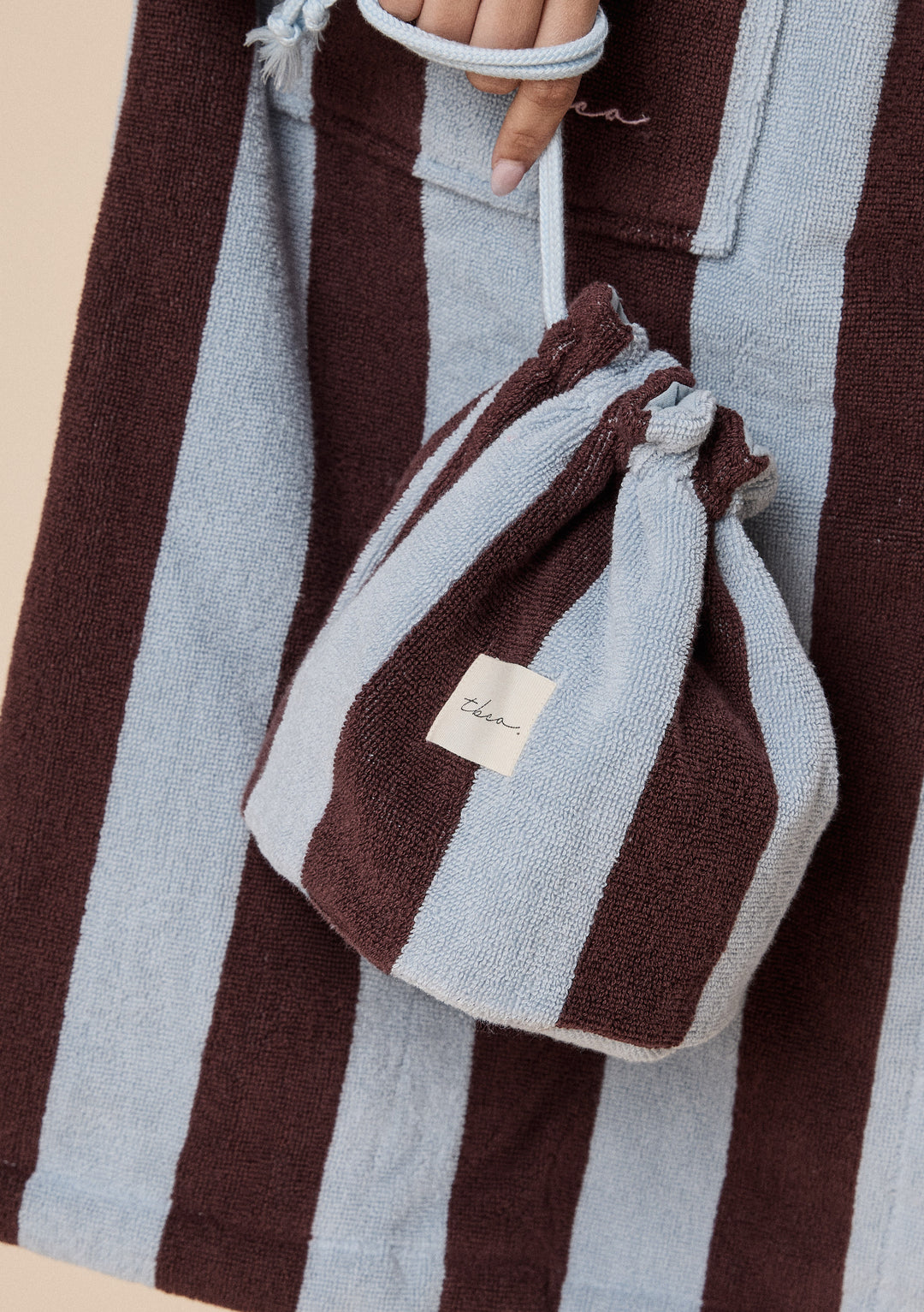 Hand holding TBCo Terry Cotton Wash Bag in Blue Stripe with soft textured sky blue and deep brown vertical bands