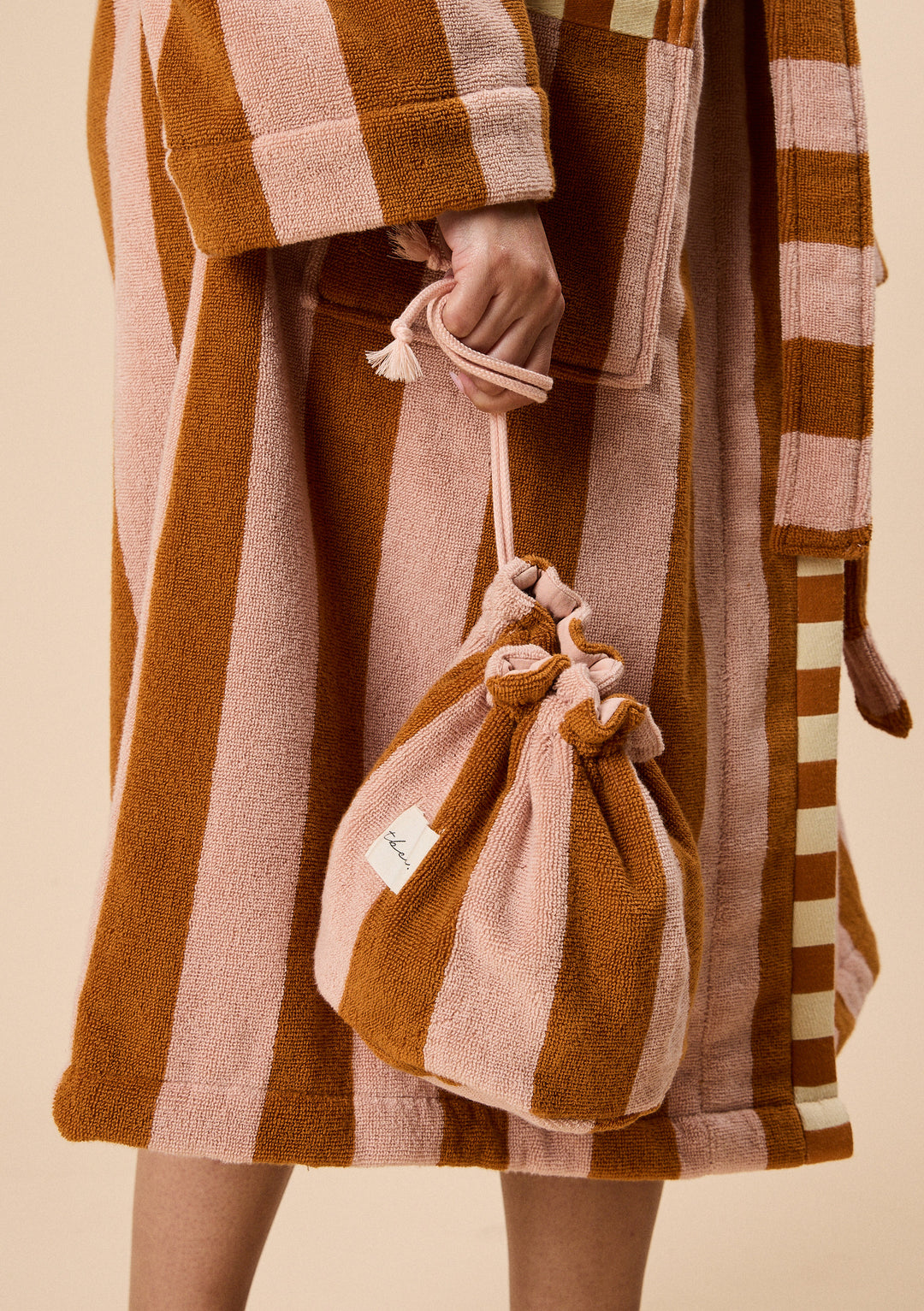 Hand holding TBCo Terry Cotton Wash Bag in Honeycomb Stripe with soft textured alternating warm brown and pink bands