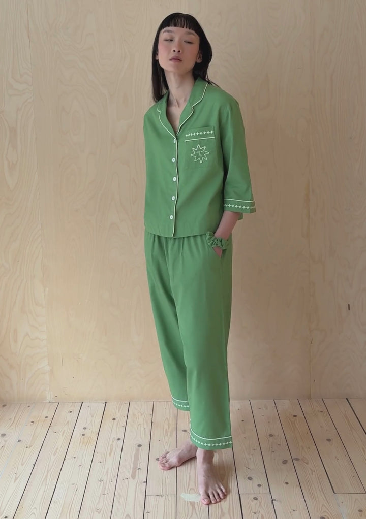 A model poses against a neutral ply backdrop, wearing a set of green TBCo cotton trouser and shirt pyjamas.