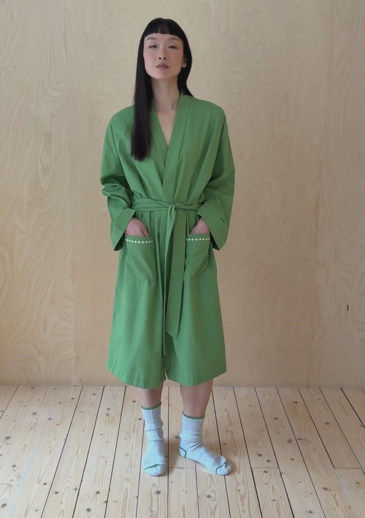A model poses against a neutral ply backdrop, wearing a TBCo green cotton robe.