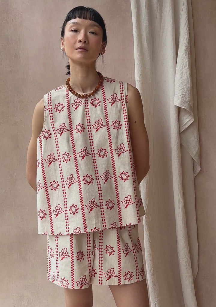 A model poses against a neutral ply backdrop, wearing a TBCo matching cream and orange floral shorts and sleeveless top set.